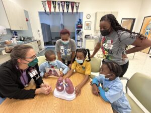Two school nurses treat 4 students. All are wearing surgical masks.
