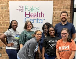 The Rales Health Team (7 adults) pose in front of the health center sign